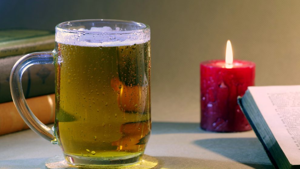 a beer or cider with a red candle in the background and the corner of an open book on the side